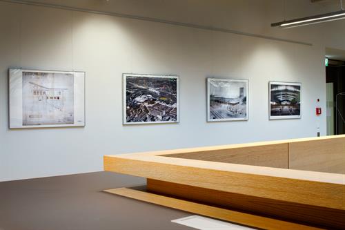 Vier großformatige Schwarz-Weiß-Fotografien hängen nebeneinander an der weißen Bibliothekswand. Sie zeigen historische Aufnahmen des Gebäudes.