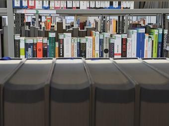 Foto: Nahaufnahme Buchregal. Blick über Bücher hinweg zu den Büchern im dahinterliegenden Regal. 