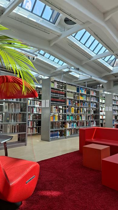 Foto: Loungebereich der BIB. Im Vordergrund Sitzmöglichkeiten mit rotem Teppich, im Hintergrund Buchregale und Blick in die Gewölbedecke.