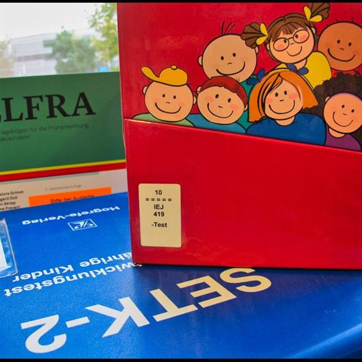 Foto: Nahaufnahme von drei gestapelten Büchern. Im Vordergrund ein Buchcover: Kinder unterschiedlicher Herkunft auf einem roten Hintergrund.  Unten liegend Cover mit SETK-2.