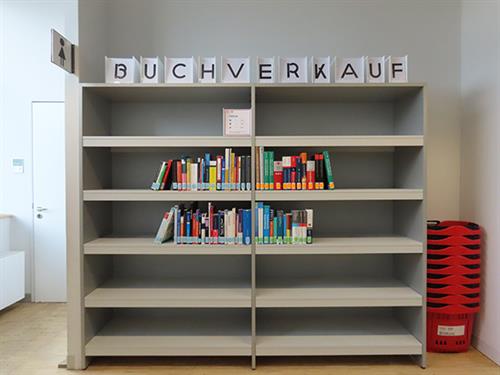 Regal mit der Beschriftung "Buchverkauf" und darin aufgestellt eine Auswahl von Literatur.