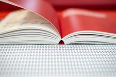 Photo: Close-up of an open book with red pages. Lying on a black and white base with numerous paragraph marks. 