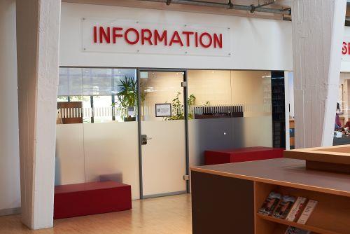 Foto: Büro der Information von außen mit geschlossener Glastür. Schild "Information" darüber, rechts und links Pfeiler. Im Büro ist Licht an und Pflanzen zu sehen.