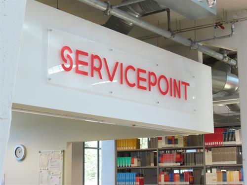 Foto: Schild Servicepoint über der Theke. Im Hintergrund Buchregale.