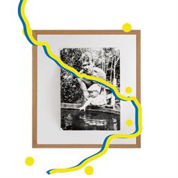 Foto: Zur Ausstellung "Pack Deine Sachen"; ein Vater hält ein Kind fest, dass in einen Pool greift; durch das Bild läuft eine gelb/blaue Linie mit gelben Punkten, wie die Markierungen auf einer Landkarte