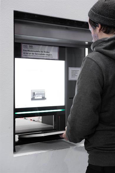 Foto: Mann in schwarzer Kleidung legt ein Buch in die Rückgabestation.