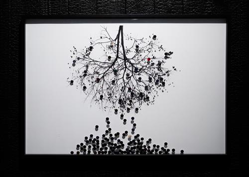 Foto der Ausstellung Seed_of_Infinity: schwarz-weiß; Baum ohne Blätter hängt verkehrt herum am oberen Bildrand und es fallen kleine schwarze und weiße Bälle aus den Ästen nach unten, so dass sich unten ein Haufen bildet;