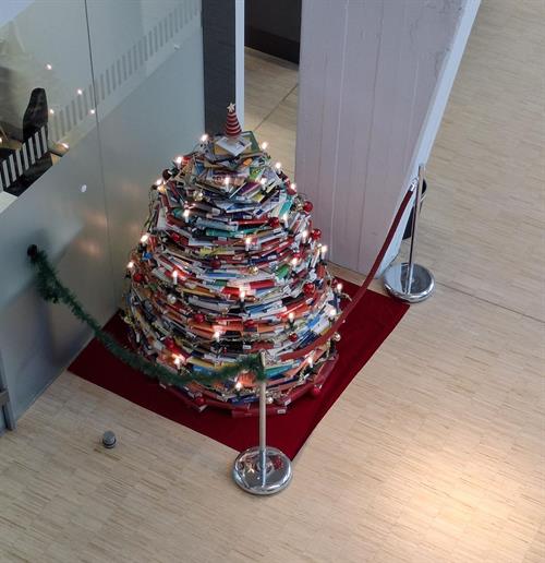 Foto: Blick von oben auf einen Weihnachtsbaum aus Büchern mit einem Stern als Spitze; Standort vor der Information, abgesperrt mit Girlanden.