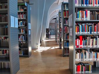 Foto: Innenaufnahme BIB. Rechts und links Buchregale mit Büchern, hinten Deckengewölbe. Sonne fällt auf das Parkett.